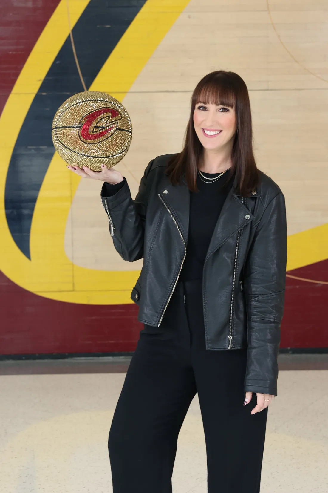 Georgia Sapounas holding a gold Cavaliers basketball in front of the Cavs logo mural