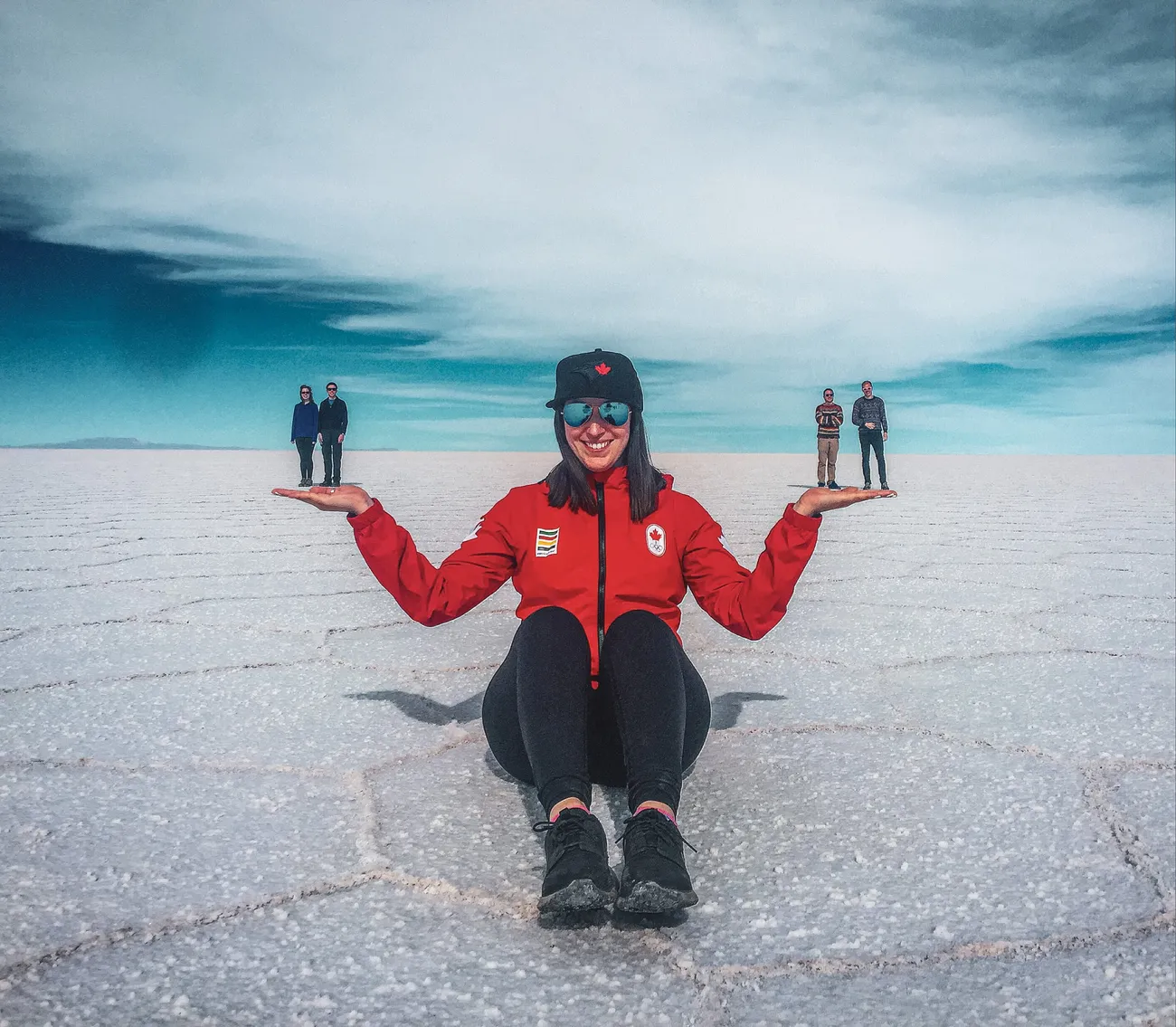 Georgia Sapounas in a Team Canada jacket on a vast salt flat, holding friends in her palms with forced perspective