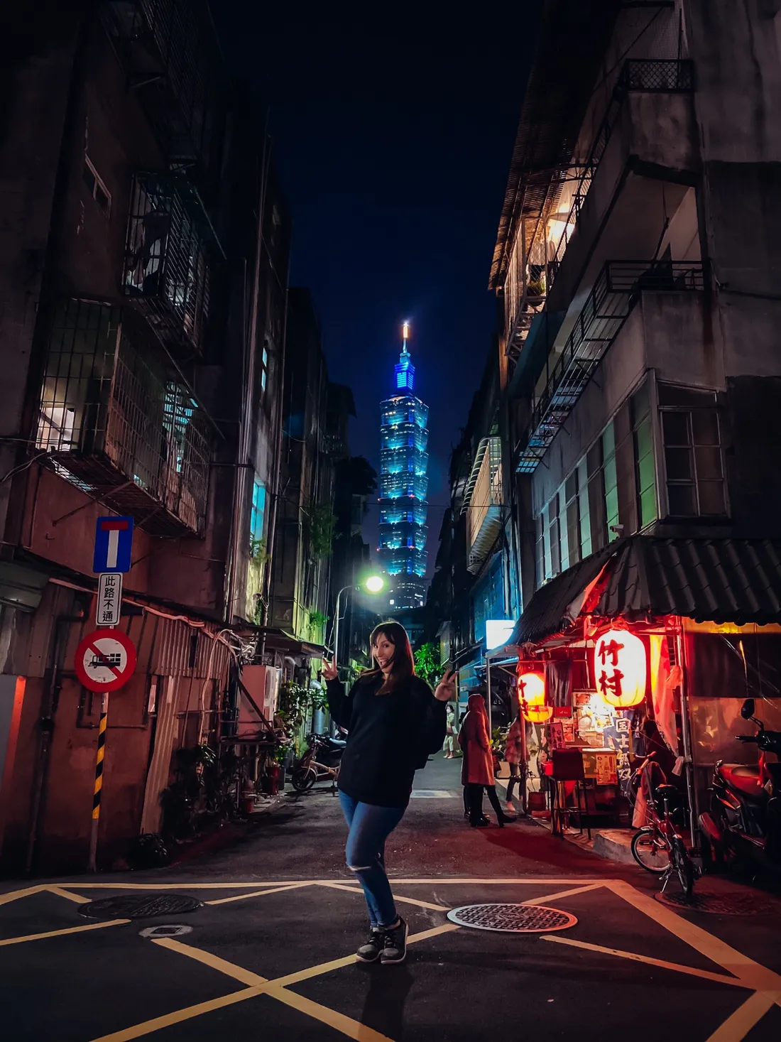 Georgia Sapounas in a Taipei alley at night with Taipei 101 glowing behind her